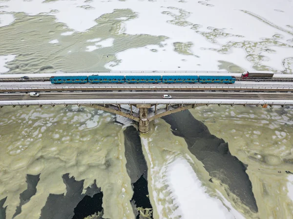 One train on Kiev metro bridge across the frozen Dnieper river. Textured pattern on ice. Aerial drone view. Winter snowy morning.