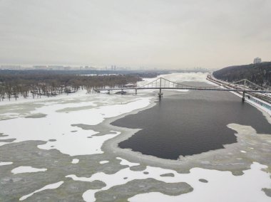 Kiev 'deki Dinyeper nehri üzerindeki kırmızı-yeşil yaya köprüsü. Nehirdeki buz kalıpları. Hava aracı görüntüsü. Kış karlı sabah.