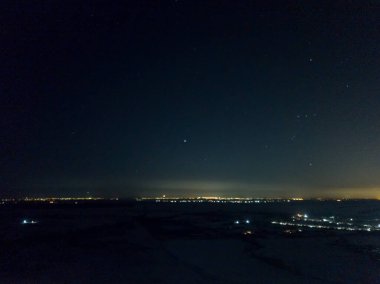 Yıldızlı gökyüzünün altındaki gece şehrinin uzak ışıkları. Hava aracı görüntüsü. Kış soğuk gece.