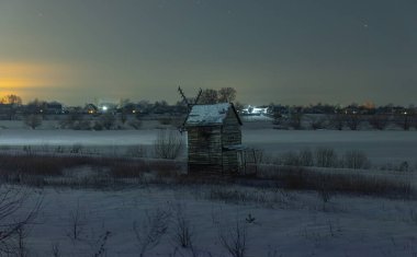 Geceleri karlı bir tarlada eski bir değirmen. Yıldızlı gökyüzü.