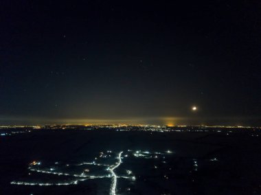 Yıldızlı gökyüzünün altındaki gece şehrinin uzak ışıkları. Hava aracı görüntüsü. Kış soğuk gece.