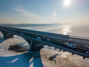 Hava aracı görüntüsü. Kiev metro treni Dinyeper nehri boyunca köprüden geçer. Kış güneşli sabah.