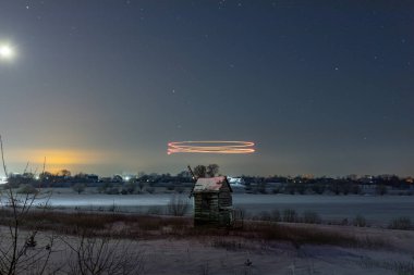 Geceleri karlı bir tarlada eski bir değirmenin üzerindeki renkli çizgiler. Yıldızlı gökyüzü. Hafif grafiti.