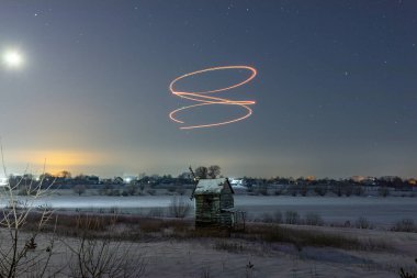 Geceleri karlı bir tarlada eski bir değirmenin üzerindeki renkli çizgiler. Yıldızlı gökyüzü. Hafif grafiti.