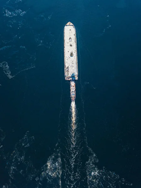 The barge floats on the freezing river. Aerial drone view. Sunny winter day, thin ice on the river.