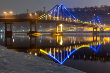 Kiev 'deki yaya köprüsü. Akşam aydınlatması. Nehirdeki köprünün yansıması..