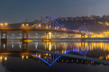 Kiev 'deki yaya köprüsü. Akşam aydınlatması. Nehirdeki köprünün yansıması..