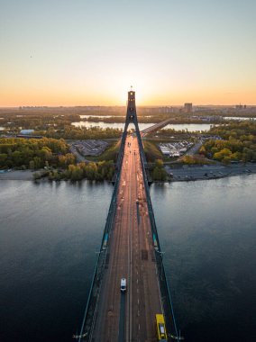 Kiev 'in kuzey köprüsü. Köprü boyunca yükselen güneş ışınları. Güneş pilonun içinden doğuyor. Hava aracı görünümü.