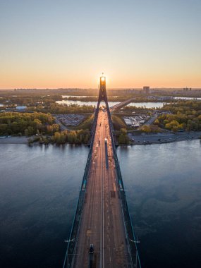 Kiev 'in kuzey köprüsü. Köprü boyunca yükselen güneş ışınları. Güneş pilonun içinden doğuyor. Hava aracı görünümü.