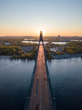 Kiev 'in kuzey köprüsü. Köprü boyunca yükselen güneş ışınları. Güneş pilonun içinden doğuyor. Hava aracı görünümü.