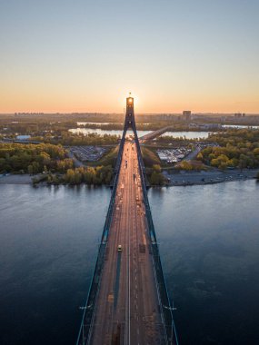 Kiev 'in kuzey köprüsü. Köprü boyunca yükselen güneş ışınları. Güneş pilonun içinden doğuyor. Hava aracı görünümü.