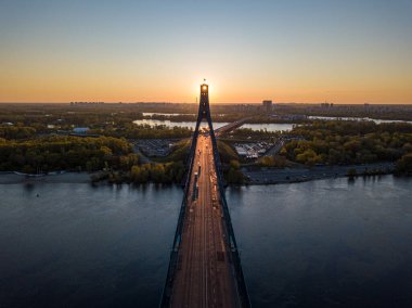 Kiev 'in kuzey köprüsü. Köprü boyunca yükselen güneş ışınları. Güneş pilonun içinden doğuyor. Hava aracı görünümü.
