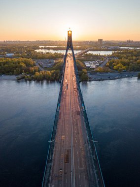 Kiev 'in kuzey köprüsü. Köprü boyunca yükselen güneş ışınları. Güneş pilonun içinden doğuyor. Hava aracı görünümü.