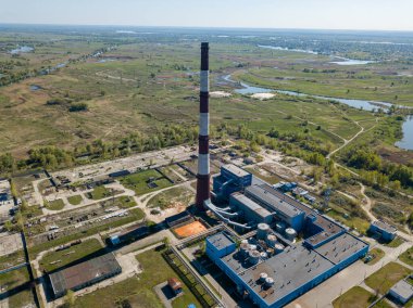 Şehrin varoşlarındaki bir elektrik santralinin yüksek bacası. Arka planda yeşil bahar bozkırları var. Hava aracı görünümü.