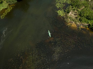 Yazın yeşil kıyıları olan dar bir nehirde kano. Hava aracı görünümü.