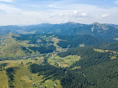 Güneşli bir yaz sabahında Ukrayna Karpatlarının yeşil dağları. Dağ yamaçlarında kozalaklı ağaçlar ve yeşil çimenler. Hava aracı görünümü.