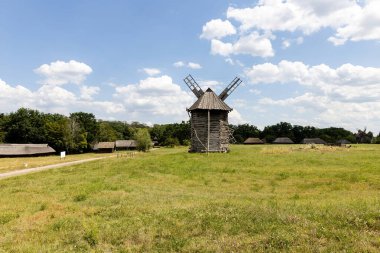 Mavi gökyüzünün altındaki yeşil alanda eski ahşap yel değirmeni