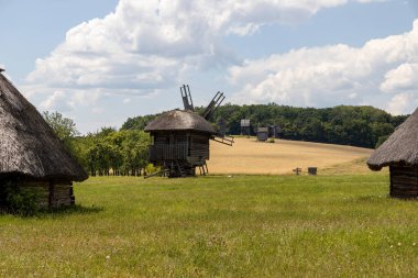 Geleneksel ahşap yel değirmenleri ve mavi gökyüzünün altındaki çimenli arazide sazdan evler