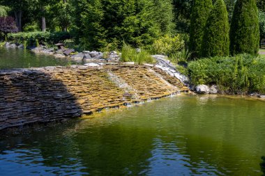 Bahçedeki yeşil gölete akan küçük taştan şelale.