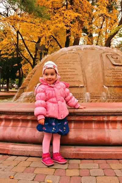 Little girl standing near fountain in autumn — Stock Photo, Image