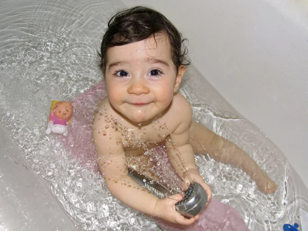 Criança pequena segurando chuveiro com salpicos na banheira — Fotografia de Stock