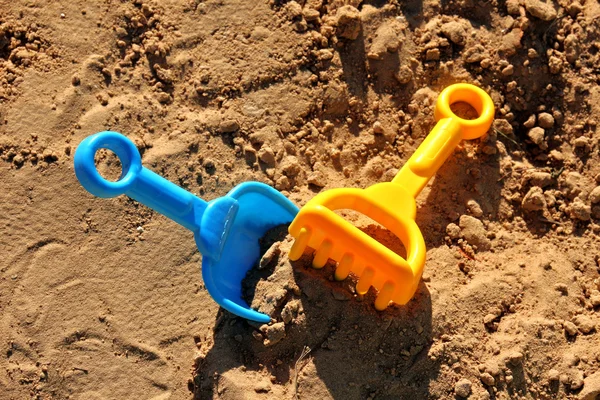 Espátula azul das crianças e ancinho amarelo, preso na areia — Fotografia de Stock