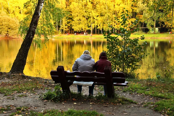 Two people on bench near lake in autumn day — Stock Photo, Image