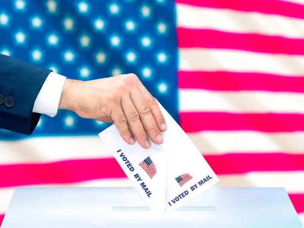A man\'s hand voting by mail in the US presidential election with the US flag behind it. Selective focus