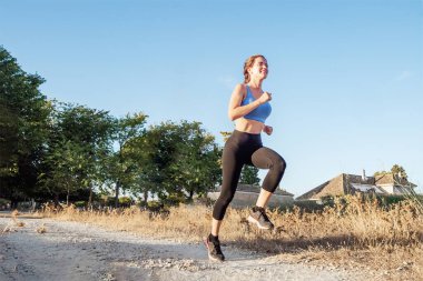 Spor giyimli genç bir kadın parkta koşuyor.