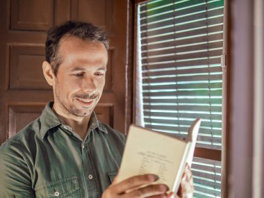 Pencerenin yanında kitap okuyan bir adam..