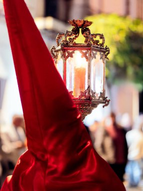 İspanya 'daki kutsal bir hafta boyunca geleneksel bir gümüş fenerin yanında kırmızı saten bir başlık takan bir tövbekârın arkasından yaklaş..