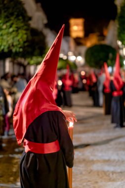 Geleneksel koyu renk bir bornoz ve uzun kırmızı bir başlık giyerek gece bir şehir caddesinde dikilen dini bir hafta geçit törenine katılan bir kişinin arka görüntüsü.