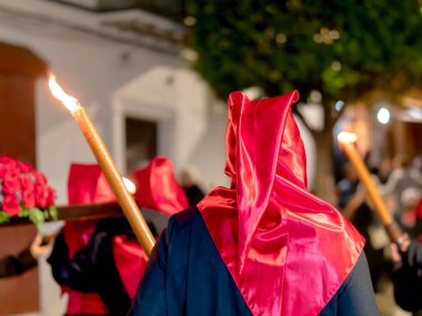 Dini bir törene katılan birinin parlak kırmızı saten bir başlık ve siyah bir bornoz giydiğini ve diğer tövbekârların uzun mumlar taşıdığını düşünün.