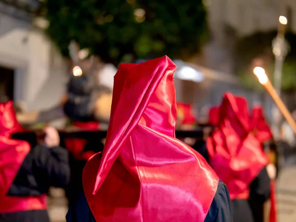 Dini bir törene katılan birinin parlak kırmızı saten bir başlık ve siyah bir bornoz giydiğini ve diğer tövbekârların uzun mumlar taşıdığını düşünün.