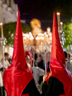 Dini bir geçit törenine katılan iki kişinin dikiz aynasından kırmızı saten başlıklar ve siyah bornozlar giyip ellerinde süslü gümüş asalar tutuyorlardı..