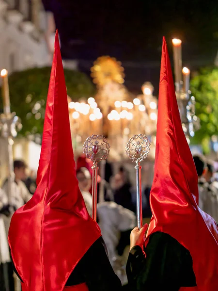 Dini bir geçit törenine katılan iki kişinin dikiz aynasından kırmızı saten başlıklar ve siyah bornozlar giyip ellerinde süslü gümüş asalar tutuyorlardı..