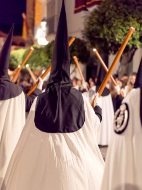 İspanya 'da geceleri düzenlenen kutsal bir törende geleneksel siyah başlıklar ve beyaz pelerinler giyen ve ellerinde mumlarla birkaç tövbekârın dikiz görüntüsü.