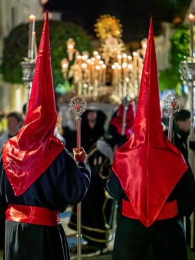 Bir grup tövbekar, geleneksel siyah cüppeli ve uzun kırmızı başlıklı, gece İspanya 'da bir şehir caddesinde düzenlenen dini bir hafta geçit töreninde...