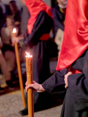 İspanya 'da düzenlenen geleneksel Kutsal Hafta geçit töreninde uzun yanan bir mum tutan kişinin yakın plan fotoğrafı. Arka planda bulanık figürler var..