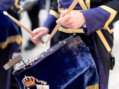 İspanya 'da geleneksel bir dini tören sırasında davul çalan mor ve altın rengi tören üniformalı bir müzisyenin detaylı görüntüsü.