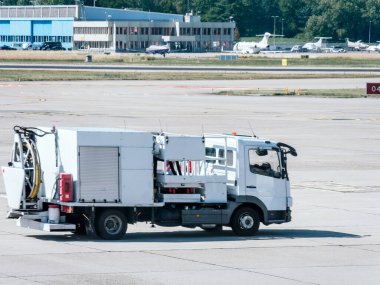Havaalanında yer destek aracı, arka planda uçaklar ve kontrol kulesi var..