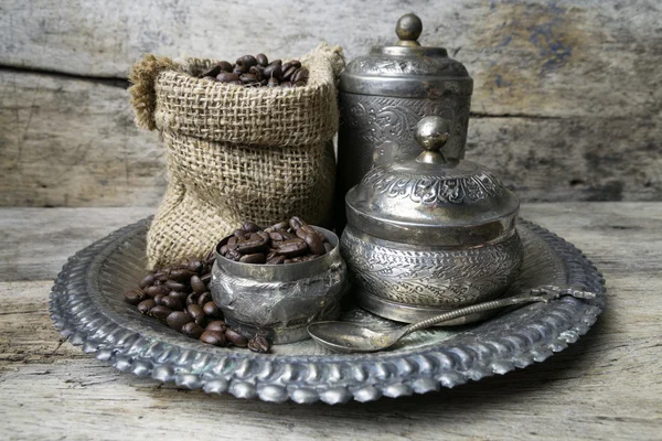銀カップと荒布バッグ木製背景がある上でのコーヒー豆 — ストック写真