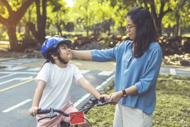 Anne kızına parkta bisiklet sürmeyi öğretiyor. Aile dışarıda bisiklet sürüyor..