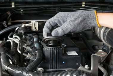 Tamirci bir otomobil motorundan yağ kapağı açıyor.