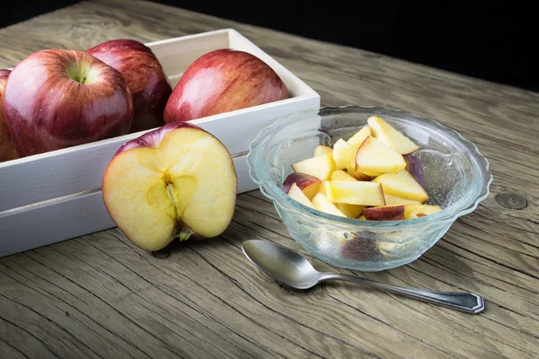 Rote Äpfel in der Schüssel und Äpfel in der Schachtel auf dem Holztisch — Stockfoto