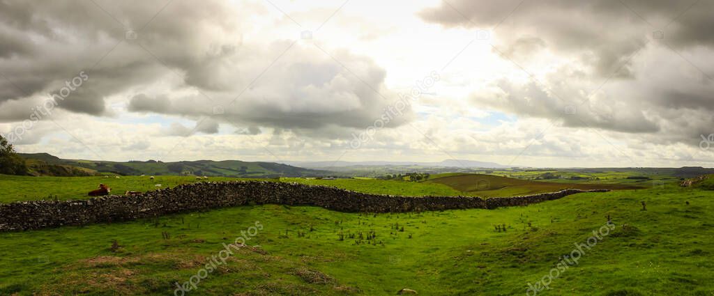 Green hills farm, and animals. English countryside, brick wall and dramatic sky panorama.