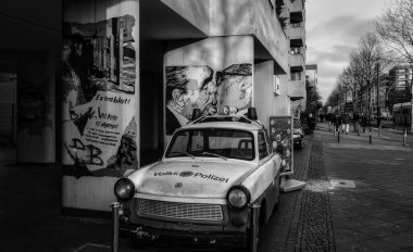B&W, iconic  Berlin history. The Socialist Fraternal Kiss graffiti, and Antique police car Trabant 601. clipart