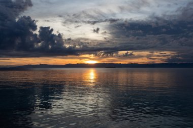 Moalboal, Filipinler 'deki sakin Pasifik Okyanusu' na simetrik olarak yansıyan altın gün batımı. Dramatik bulutları ve huzurlu bir akşam atmosferi olan sakin bir tropikal deniz manzarası..