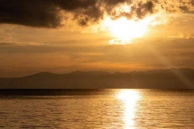 Moalboal, Filipinler 'de Pasifik Okyanusu' nda dramatik bir altın gün batımı. Güneş ışığı bulutları delip geçiyor ve sakin tropikal sularda yansıyor..