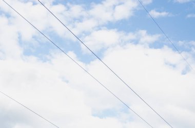 Beyaz bulutlu açık mavi gökyüzüne karşı güç hatları.